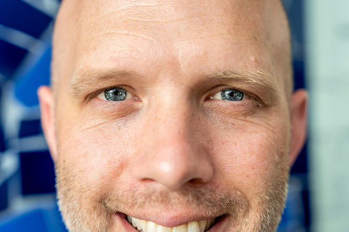 Portrait of a bald man with blue eyes looking optimistic with a blue ceramic background.