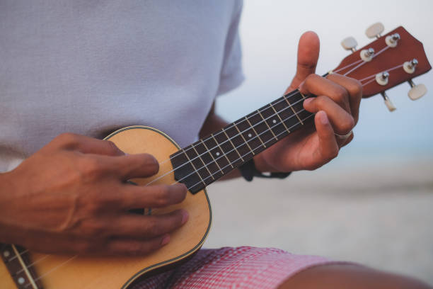 istock Close up a man playing guitar ukulele on the beach with light effect. 1415740132
