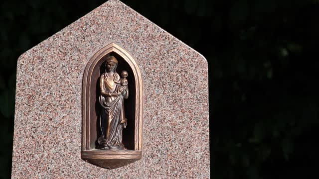 Blessed virgin mary statue with Jesus Christ as baby on a cemetery graveyard or gravestone shows holy madonna as sacral memorial and sacred figurine in catholic religion is saint figure on many graves