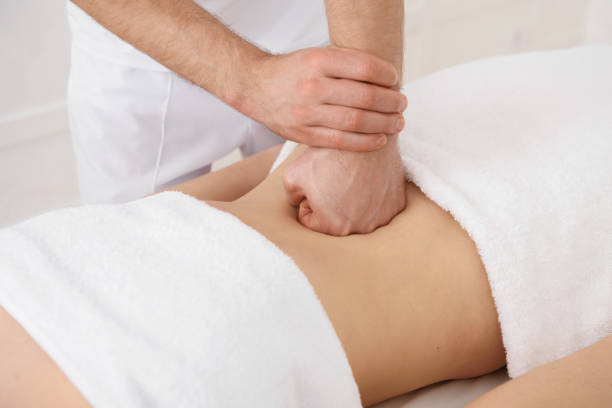 Close up of osteopath doing manipulative massage on woman abdomen on white background, copy space stock photo