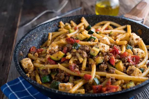 Delicious homemade cooked one pan dish, greek style food with macaroni, ground beef, feta cheese and mediterranean vegetables. Served ready to eat isolated on wooden table