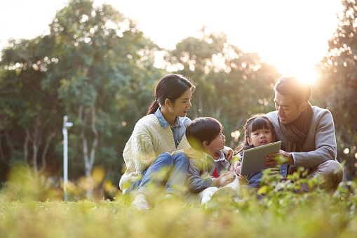 asian family with two children relaxing outdoors in city park