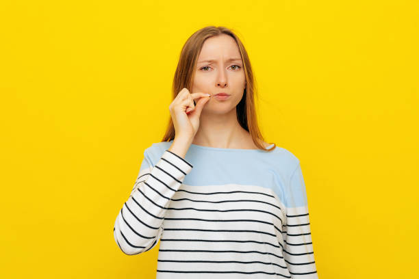 Serious girl mouth and lips shut as zip with fingers asking conceal some private confidential information, standing in striped sweatshirt over yellow background. Secret and silent, taboo talking Serious girl mouth and lips shut as zip with fingers asking conceal some private confidential information, standing in striped sweatshirt over yellow background. Secret and silent, taboo talking speak no evil stock pictures, royalty-free photos & images