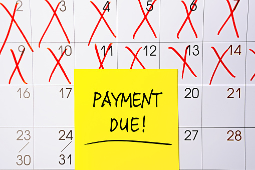 The phrase Payment Due written in black text on a yellow sticky note posted to a calendar page as a reminder. Close up of a personal agenda, top view. Motivational quote