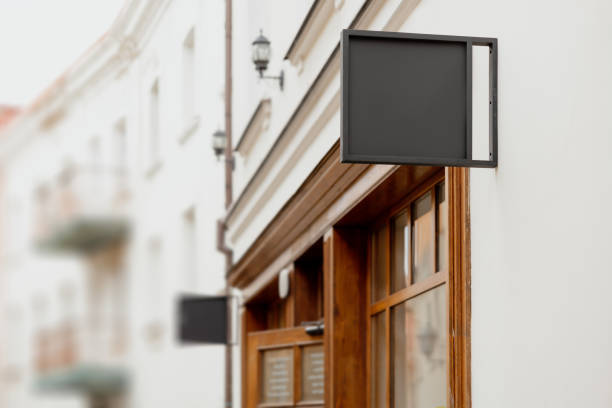 istock Blank signboard mock up, on the facade. Copy space for your store sign or logo. Modern empty outdoor signage, mockup to add company logo. Black square store signboard on white wall. 1415754408