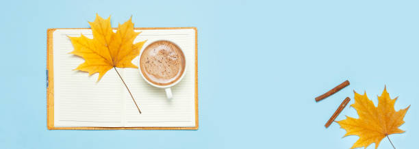 istock Opened notebook, cocoa latte or coffee in cup, yellow autumn maple leaf on blue background top view flat lay. Autumn or winter hot drink, concept of study, working table. Long banner Space for text 1415754460
