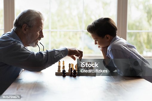 istock Elderly granddad teaching little boy grandkid to play chess game 1415754674