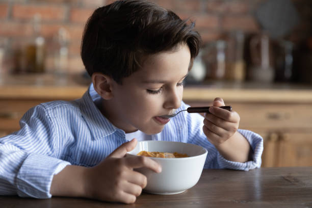 préadolescent affamé ayant un bon appétit en mangeant des céréales avec du lait - bon appetite photos et images de collection