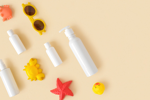Sunscreen lotion tube on neutral background. Plastic bottle of sun protection and kids sunglasses and sandbox toys on beige table. Children skin care concept. Sunscreen for children. Baby Cosmetic.