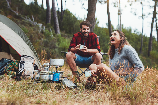 Happy young couple laughing together while sitting outside their camping tent. Cheerful young couple enjoying themselves on a camping holiday.