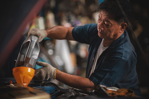 A man pouring oil to the Engine at Auto Repair Shop.