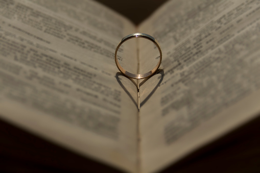 Wedding ring with a falling shadow in the form of a heart standing on an open book...
