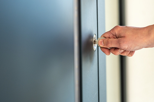 Close-up of mature man's hand unlocking door with key to enter his house.