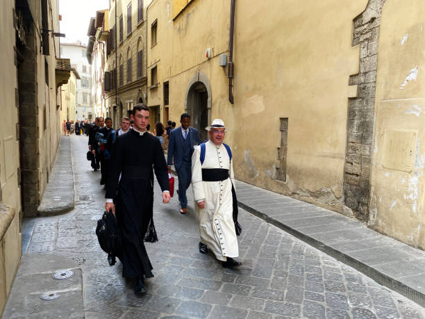 sacerdote con una sotana blanca y los seminaristas vestidos de negro caminando por las calles de florencia - sotana fotografías e imágenes de stock