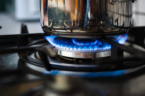 Close up color image depicting a cooking pan on a gas hob with blue flames in the kitchen.