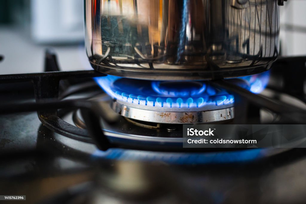 Cooking on gas hob in kitchen with blue flames burning Close up color image depicting a cooking pan on a gas hob with blue flames in the kitchen. Gas Stove Burner Stock Photo