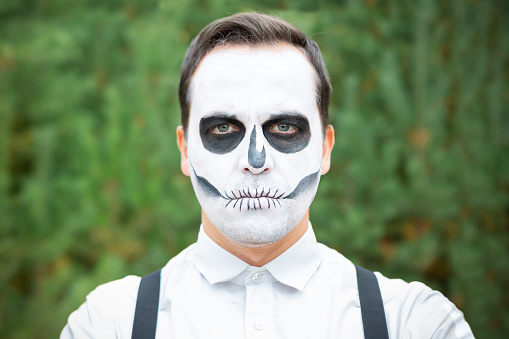 A young man with a skeleton makeup stands in the woods. Halloween party