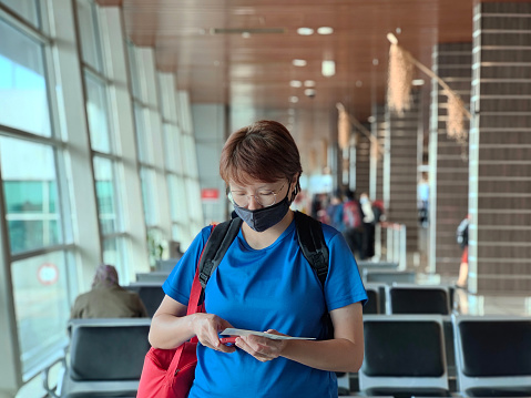 An Asian woman is wearing cloth mask at the airport ready for flight departure.