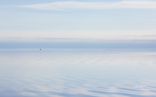 Pale lilac blue sky reflected in the calm smooth lake surface. Ethereal evening seascape in pastel colors with copy space. Atmosphere of serenity and tranquility. Russia, Vologda Oblast, Lake Beloye.
