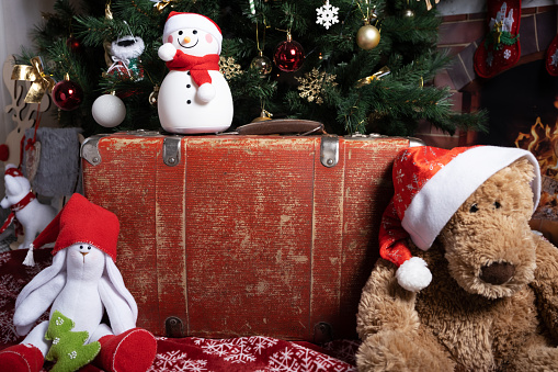 On a red old suitcase sits a snowman and next to a toy bear in a Santa Claus hat.
