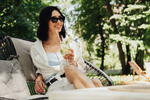istock Young Brunette Woman Relaxing and Drinking Cocktail While Sitting on Restaurant Terrace Outdoors in Summer Sunny Day 1415773891