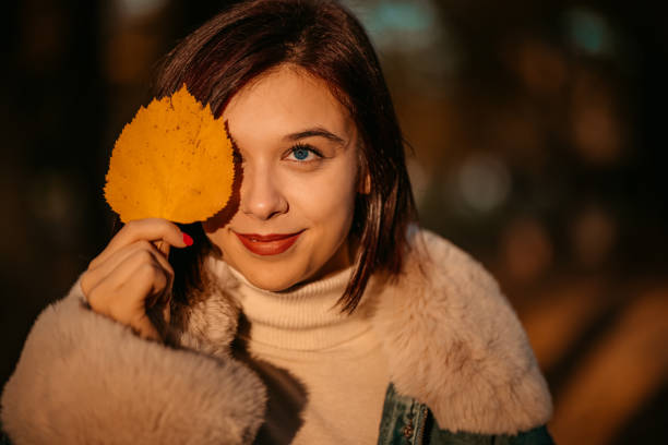 Beautiful young woman in a public park during autumn. Holding a leaf.