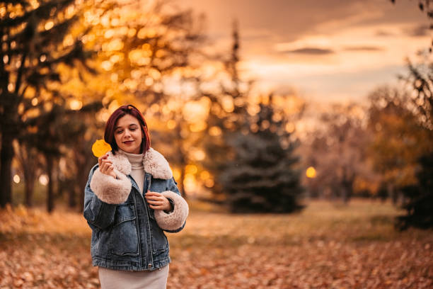 Beautiful young woman in a public park during autumn. Holding a leaf.