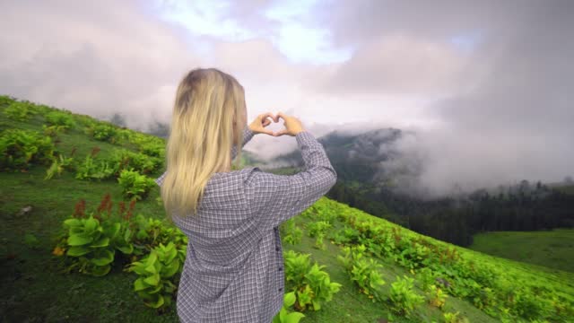 Young girl makes her fingers and hands heart in mountains.