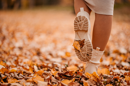 Close-up of young woman's boots, standing on autumn leaves in the park.