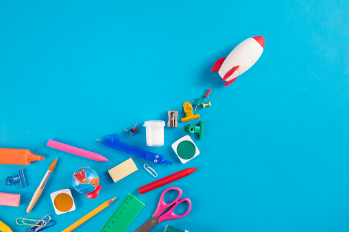 Trail of school supplies behind a space rocket on blue background
