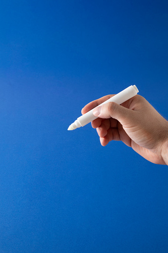 Human hand is holding white felt tip pen on blue background