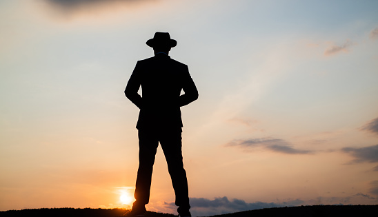 silhouette of man in hat standing on sunrise sky, loneliness.