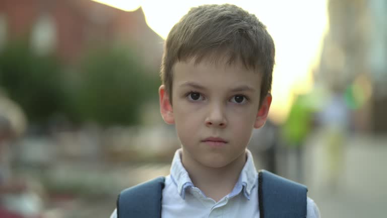 Close-up portrait of a boy with a backpack outdoors looking at the camera.