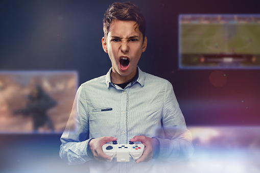The concept of video games. Teen screams during video game. In the hands of holds joystick. Dark background. In front of his face transparent screens with video games.