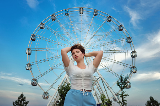 Young woman posing in city park near Ferris wheel.