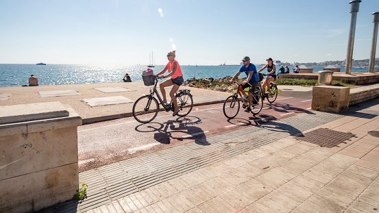 October 24, 2018 - Palma de Majorca, Balearic Islands, Spain, Europe: people walking at the street in sunny weather. Palms, beach cycling road. Person riding cycle outdoors.
