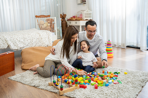 Happy young father and mother and a little daughter playing with Toy wooden blocks, sitting on the floor in living room, family, parenthood and people concept with Developmental toys