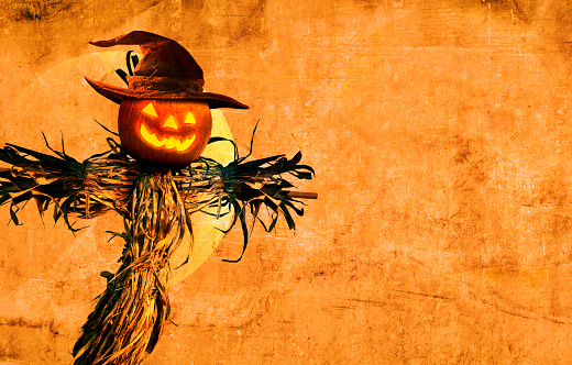 A jack o'lantern sits on top of a scarecrow in front of an orange grunge background.