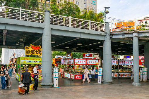 Xi'an, China - July 20, 2022: People walking and standing in an area with free-standing shopping kiosks. The kiosks have bold and colorful signs in Chinese characters