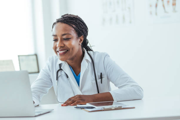 Concentrated afro american woman doctor using laptop while sitting at workplace in medical clinic