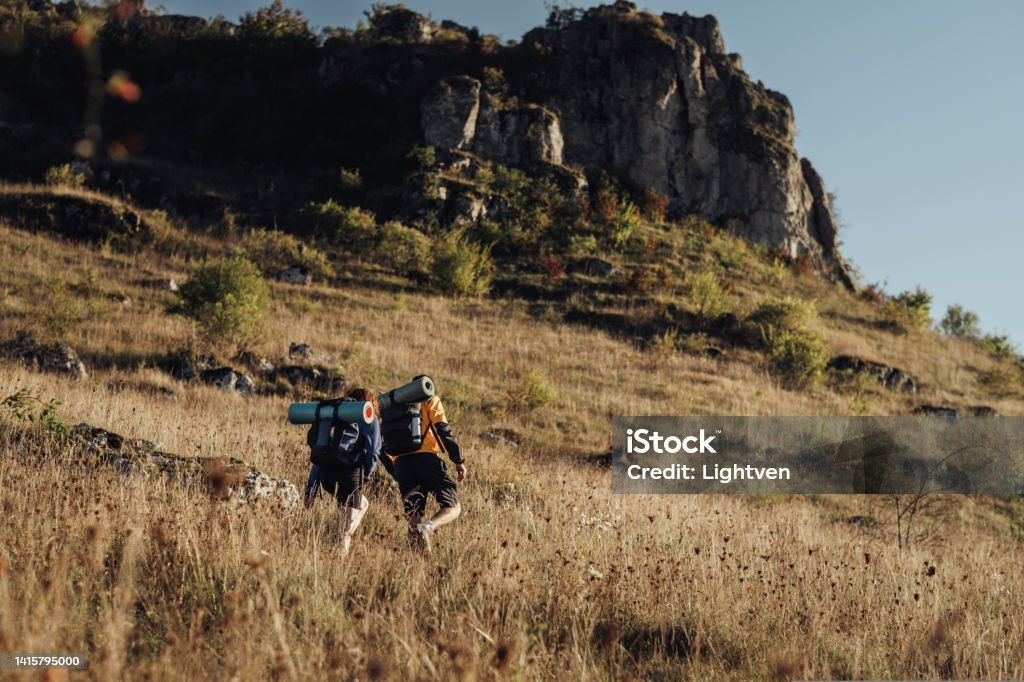 Two Hikers Moving on Their Route on Top of Hill During Sunset, Travel Couple Enjoy Hiking Trip Two Hikers Moving on Their Route on the Top of Hill During Sunset, Travel Couple Enjoy Hiking Trip Active Lifestyle Stock Photo