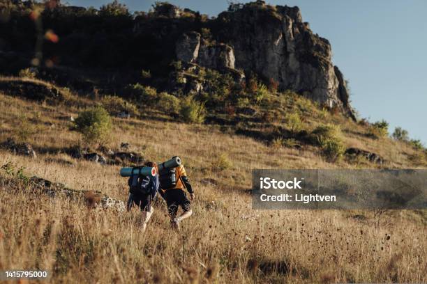 Two Hikers Moving On Their Route On Top Of Hill During Sunset Travel Couple Enjoy Hiking Trip Stock Photo - Download Image Now
