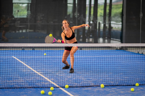 Woman playing padel in a blue grass padel court indoor - Young sporty woman padel player hitting ball with a racket Woman playing padel in a blue grass padel court indoor - Young sporty woman padel player hitting ball with a racket paddle ball stock pictures, royalty-free photos & images