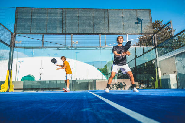 partido de pádel mixto en una pista de pádel de hierba azul 
hermosa chica y hombre guapo jugando al pádel al aire libre - tennis in a row team ball fotografías e imágenes de stock