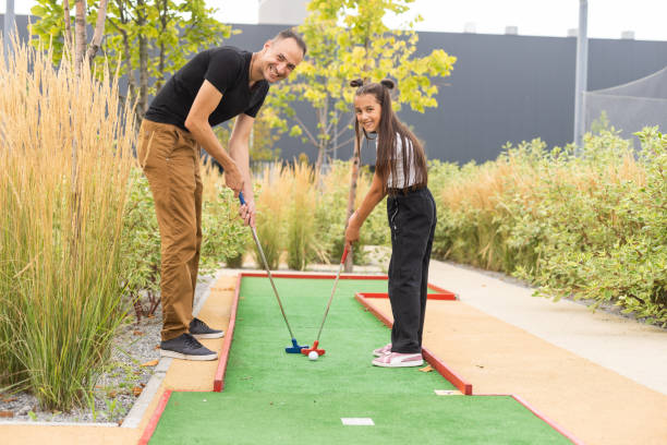 istock Sharing with golf experience. Cheerful young man teaching his daughter to play mini golf at the day time. Concept of friendly family 1415799990