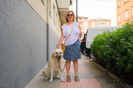Mature woman looks at the camera with her dog in the street