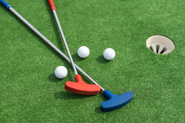 istock Assorted miniature golf putters and balls askew on synthetic grass. 1415802349