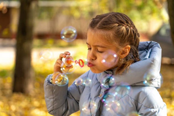 Caucasian little girl blowing soap bubbles outdoors at autumn morning. Happy carefree childhood, lifestyle concept. stock photo