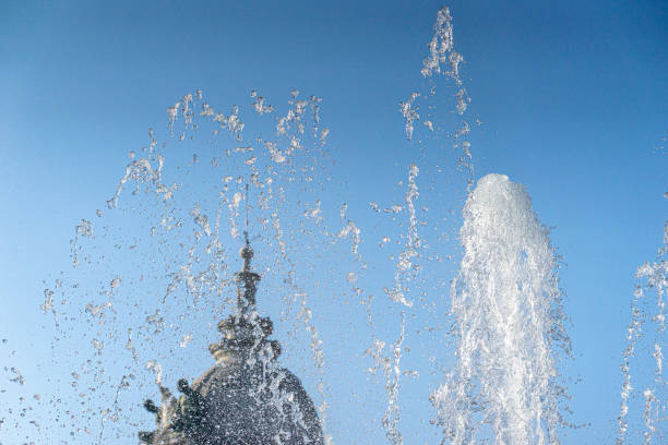Jets and splashes of water from a fountain against a blue sky backlit by a bright summer sun
