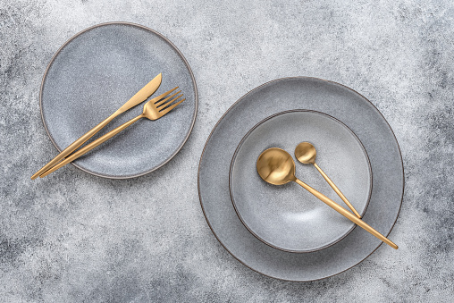 Gray plates and golden cutlery, gray grunge background. Dishes for table setting. Modern craft ceramics. Top view, flat lay.